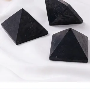 Closeup of polished black stone pyramid ornaments on white cloth for home decor and degaussing.