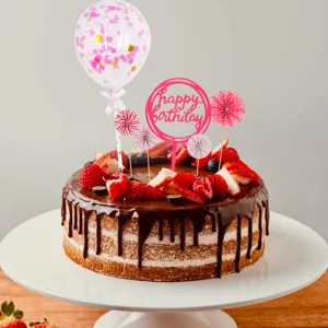 Close-up detail of pink birthday cake topper set featuring balloon, paper fans and cute sign.
