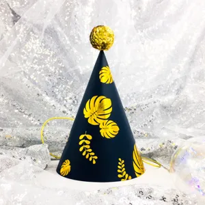 Close-up detail of a black and gold tropical leaf birthday party hat with a shiny pompom.