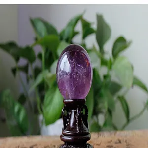 Detailed close-up view of a polished purple amethyst crystal egg on a fine wooden stand.