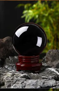Black obsidian crystal sphere detail shot with wooden base, polished feng shui stone decor.
