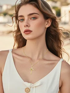 Close-up detail of a delicate gold cross necklace with heart gemstone on a model.