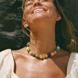 Gros plan d'un collier court en perles de résine colorée et boule dorée, bijoux de cou élégants.