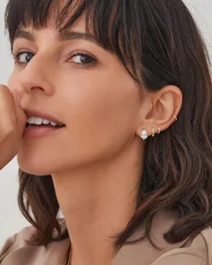 Close-up detail of stylish gold plated pear cubic zirconia earrings and minimalist huggie hoops.