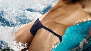 Close-up detail of men minimalist T-back string swim brief in splashing water scene.