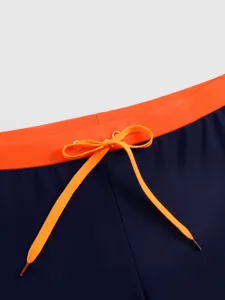 Men's swim trunks detail shot showing contrast orange waistband and matching adjustable drawstring.