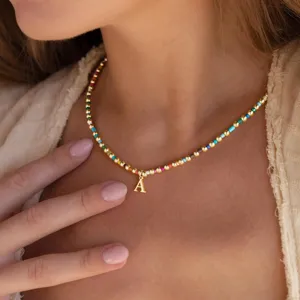 Detailed close-up of a colorful beaded necklace featuring a shiny gold letter A pendant worn on neck.