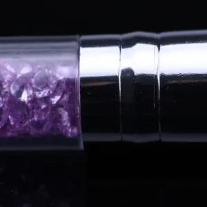 Gros plan de pinceau à poussière d'ongles avec manche transparent rempli de strass violets.