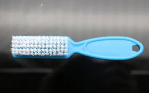 Close-up detail view of a blue plastic nail cleaning brush featuring durable white bristles.