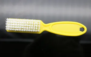 Yellow plastic nail cleaning brush detail, featuring dense white hard bristles and hole.