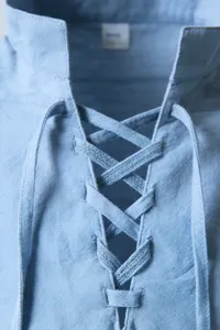 Close-up detail of light blue men's vintage lace-up collar shirt showing fabric and strings.