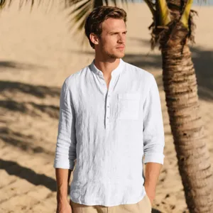 Detailed view of white linen long sleeve mandarin collar shirt worn on beach scene.