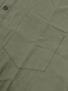 Primer plano del tejido de la camisa de lino verde, bolsillo en el pecho y detalle de botón.