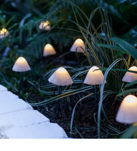 Detailed shot of outdoor LED solar mushroom pathway lights glowing warm in garden grass.