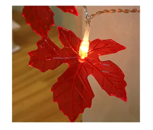 Close-up detail of red artificial maple leaf LED string light with warm glowing light.