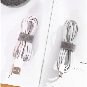 Graue Klettverschluss Kabelbinder organisieren weiße Ladekabel auf einem sauberen Schreibtisch.