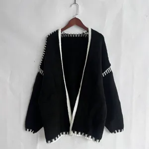 Detail view of black knitted cardigan with white trim, cozy long sleeve casual sweater apparel.