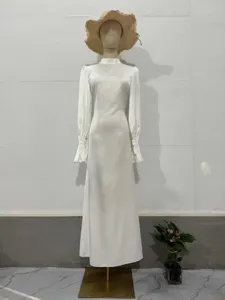 Elegante witte maxi-jurk met lange mouwen, hoge hals en gerimpelde manchetten.