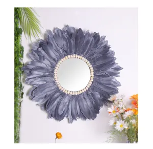Dettaglio specchio da parete boho in piume, con conchiglie naturali e morbide piume grigie.