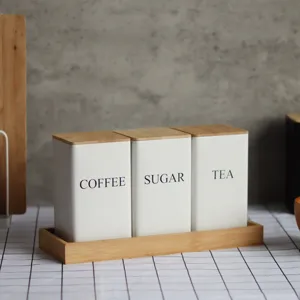 Close up of white metal storage canisters with bamboo lids and tray for coffee, sugar and tea.