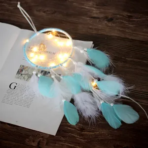 Gros plan détaillé du attrape-rêves lumineux avec plumes bleues et guirlande LED sur table.
