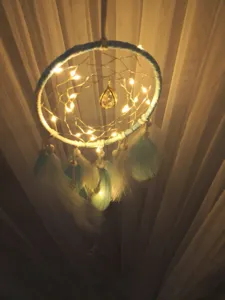 Gros plan d'attrape-rêves bleu avec guirlande lumineuse, plumes et pendentif en cristal.