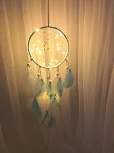 Attrape-rêves suspendu avec guirlande lumineuse et plumes pour décoration de chambre chaleureuse.