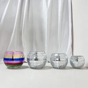 Detail shot of silver and colorful mosaic disco ball candle holders set against white fabric.