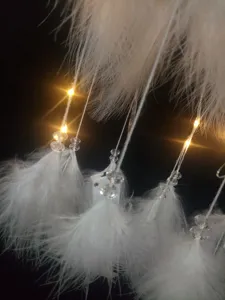 Detailaufnahme des handgefertigten Traumfängers mit weißen Federn, warmen LEDs und Kristallen.