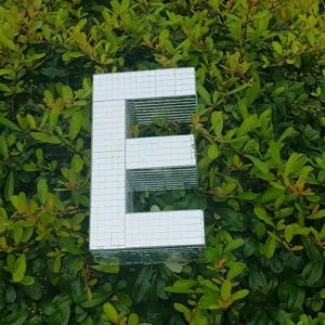 Close-up of a 3D disco mirror letter E decor, placed on green leaves for party display.