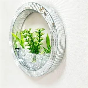 Close up of round mosaic mirror wall hanging glass vase with artificial green plants inside.
