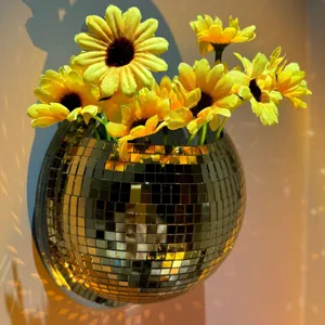 Nahaufnahme eines goldenen Diskokugel-Wandpflanzers mit gelben künstlichen Blumen an Wand.