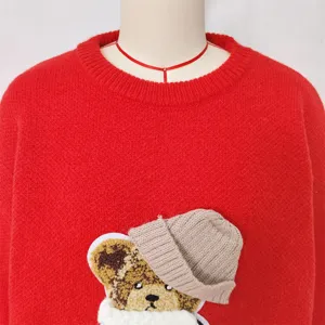 Detail van een rode gebreide trui met een schattige 3D teddybeer patch en warme muts.