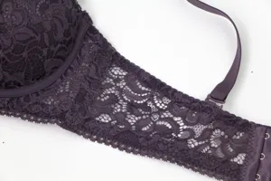 Close-up view of dark purple lace bra wing, detailed floral pattern texture, elastic strap.