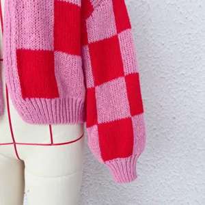 Détail de gilet tricoté à carreaux rose et rouge, texture de pull épais, style automnal douillet.