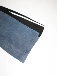 Close-up view of spliced denim trousers featuring black side panels and white stripes.