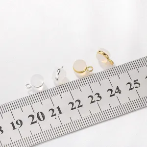 Close up view of small round jewelry charms with metal bails shown with ruler for scale reference.