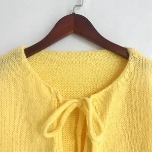 Vista detallada de un cárdigan de punto amarillo con cuello redondo y lazo frontal.