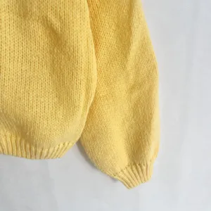 Vista detallada del suéter de punto amarillo para mujer, con textura suave y puños.