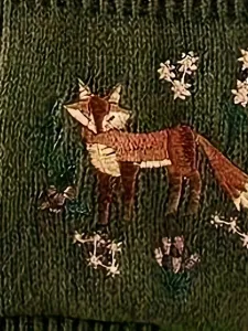 Détail de pull en tricot avec motif de renard et de fleurs, texture douce en gros plan.