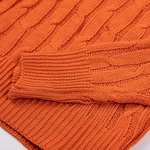 Close up of orange cable knit sweater fabric showing soft texture and ribbed cuff detail.