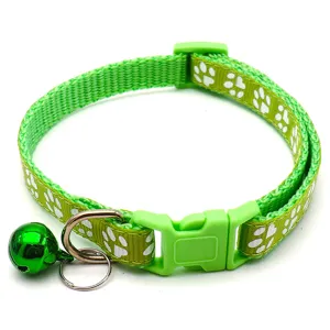 Close-up detail of green pet collar with white paw prints, buckle, and metal bell.