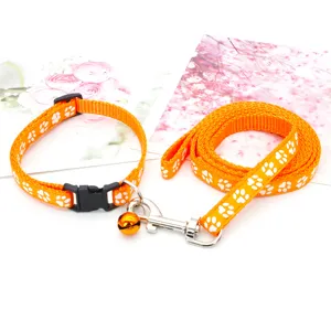 Set collare e guinzaglio per animali arancione con impronte di zampe bianche e campanello.