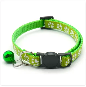 Close-up detail of green pet collar with white paw prints, safety buckle and ringing bell.