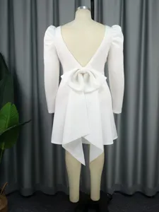 Detailaufnahme des weißen langärmligen Kleides mit rückenfreiem Design und großer Schleife.