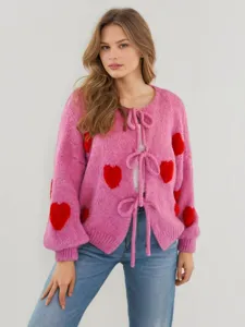 Roze gebreid vest met rode hartjespatronen, lange mouwen en strikbandjes aan de voorkant.