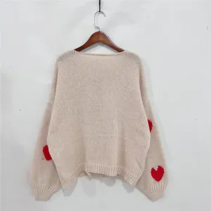 Gedetailleerd overzicht van het beige gebreide vest met rode hartborduursel en lange mouwen.