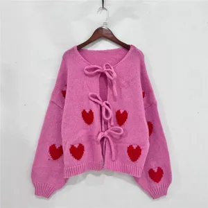 Gedetailleerd overzicht van het roze gebreide vest met rode hartjesmotieven en strikken.