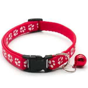 Gros plan détaillé du collier pour animal en tissu rouge avec motifs de pattes blanches et clochette.