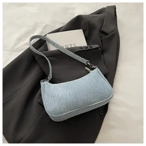 Detail shot of a light blue denim shoulder bag resting on a dark blazer and aesthetic book.